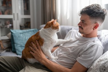 Genç adam ve kahverengi kedi oturma odasında birlikte oynuyorlar.