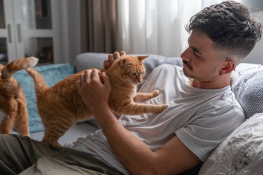 Genç bir adamın göğsünde duran kahverengi tekir kedi.