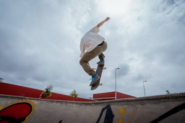 Genç kaykaycı kaykay parkında bir kasenin üzerinden atlıyor.