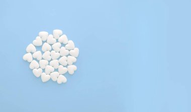 Pastel mavi arka planda kalp şeklinde beyaz haplar ve kopyalama alanı.