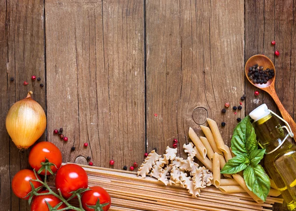 Pastas, tomates, cebolla, aceite de oliva y albahaca sobre fondo de madera — Foto de Stock