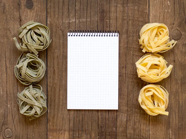 Pasta and notebook on old wooden table — Stock Photo, Image