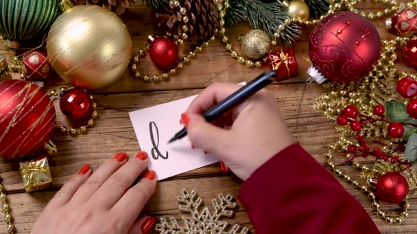 女人的手在靠近圣诞装饰的地方写12月的卡片女人的手在木制桌子上写12月的卡片 上面写着圣诞 — 图库视频影像