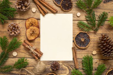 Kış Noel Kompozisyonu ve tahta masa üzerinde boş bir kart. Noel ve Yeni Yıl tebrik kartı şablonu köknar ağacı dalları, çam kozalakları ve süslemelerle dolu. Tatil modeli.