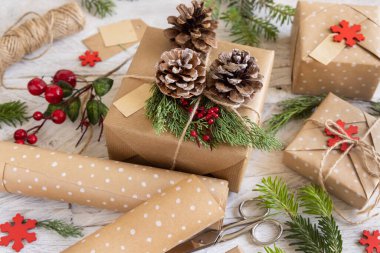 Beyaz arka planda çam kozalakları ve ardıç dallarıyla süslenmiş paketlenmiş Noel hediyesi. Boşluğu kopyala