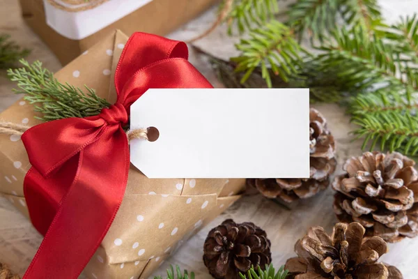 クリスマスには モミの木の枝 松のコーン 休日の装飾が閉じられた紙のギフトタグでプレゼントを包んだ 空白のギフトタグ付きの素朴な冬の組成モックアップ コピースペース 閉じる — ストック写真