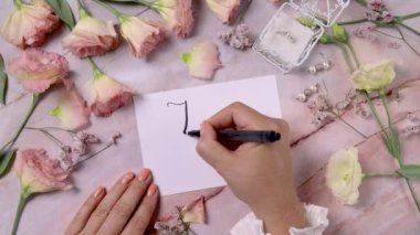 Hands writing JUST MARRIED on a card near pink flowers close up on a marble table