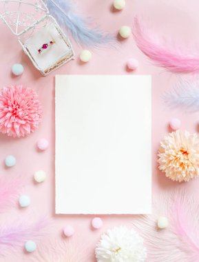 Pastel çiçeklerin yanındaki boş kart, ponpon kızlar, tüyler ve açık pembe üst manzaralı bir hediye kutusunda yüzük. Dikey kâğıt maketli romantik sahne, metin yeri, düz yatak. Sevgililer Günü, Bahar ya da kız işi konsept