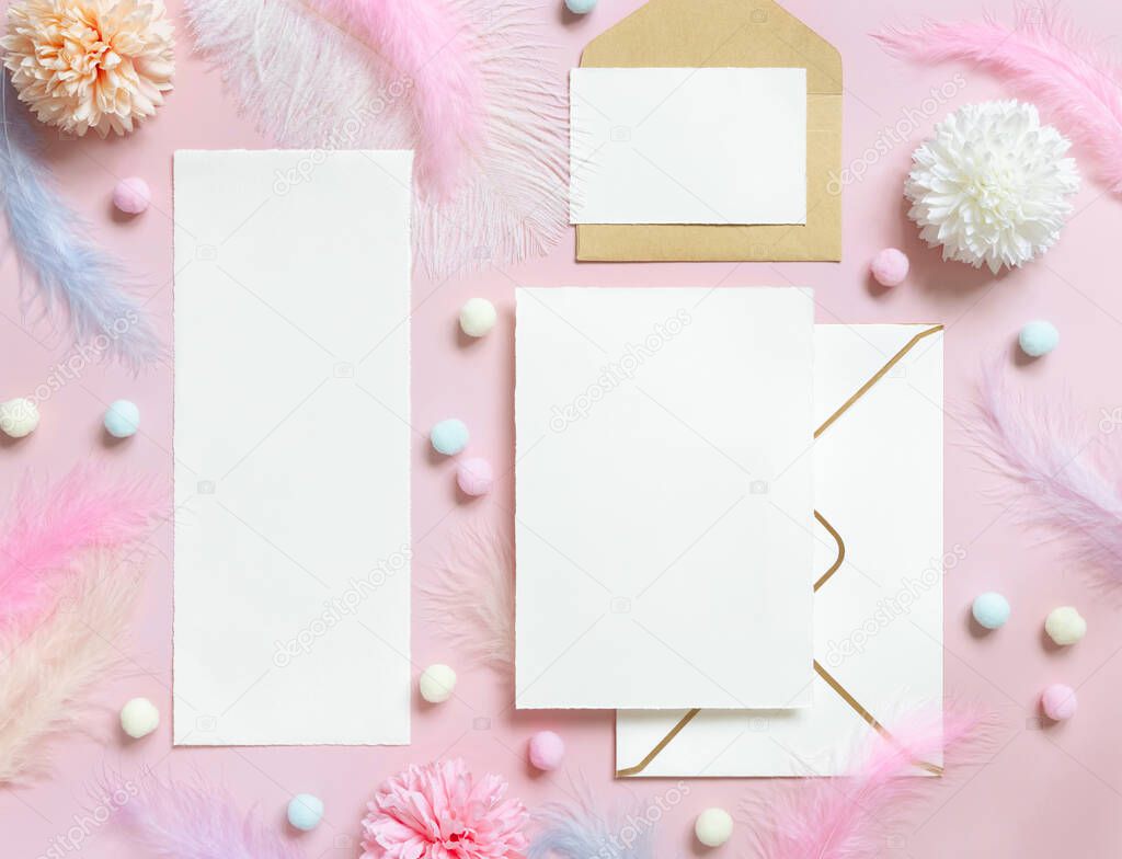 Blank cards and envelope near pastel flowers, pom-poms and feathers near ring in a gift box on pink top view. Romantic scene with wedding stationery, place for text  flat lay. Valentines, Spring or girlish concept