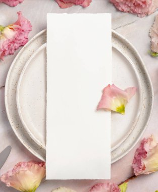 Düğün menüsü, çiçeklerle ve kurdelelerle süslenmiş mermer bir masada seramik bir tabakta duruyor. Boş kağıt tebrik kartlarının olduğu bir sahne. Dişi düz uzanış