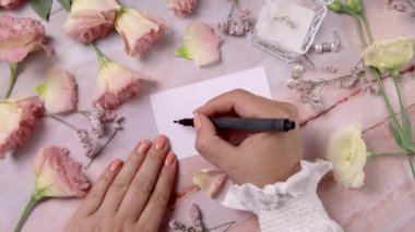 Pembe çiçeklerin yakınındaki bir karta gülümseyen eller mermer bir masaya kapanır.