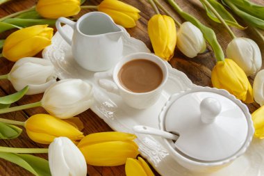 Beyaz ve sarı lalelerin yakınındaki zarif kahve tepsisi ahşap masanın üzerinde. Romantik kahvaltı.