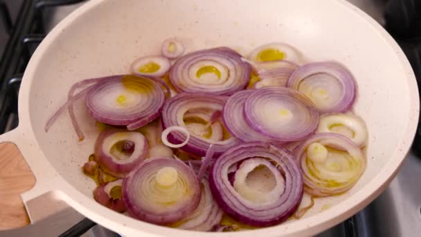 加熱されたオリーブオイルと白フライパンでスライスされた生の紫色の玉ねぎをフライアップズームイン — ストック動画