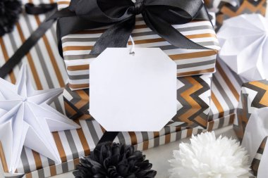 Boş hediye etiketi ve siyah fiyonk var. Çizgili ve simge geometrik kağıda sarılı hediye kutuları, siyah ve beyaz dekorun yanında. Noel, Yeni Yıl, Doğum günü, Yıldönümü Modeli