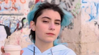 Mavi kapüşonlu genç kız kahve içiyor. Mavi saçlı genç kız dışarıda grafiti duvarının yanında kalıyor. Modelleme, kafadan vur. Hipster ve ergenlik kavramı