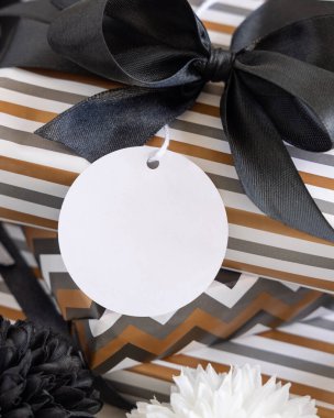 Boş yuvarlak hediye etiketi ve siyah fiyonk var. Çizgili ve simge geometrik kağıda sarılı hediye kutuları, siyah ve beyaz dekorun yanında. Noel, Yeni Yıl, Doğum günü, Yıldönümü Modeli