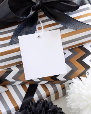 Üzerinde boş kare hediye etiketi ve siyah fiyonk var. Çizgili ve simge geometrik kağıda sarılı hediye kutuları, siyah ve beyaz dekorun yanında. Noel, Yeni Yıl, Doğum günü, Yıldönümü Modeli