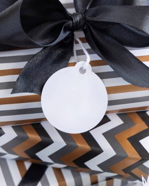 Yuvarlak boş hediye etiketi ve siyah fiyonk var. Çizgili ve simge geometrik kağıda sarılı hediye kutuları, siyah ve beyaz dekorun yanında. Noel, Yeni Yıl, Doğum günü, Yıldönümü Modeli