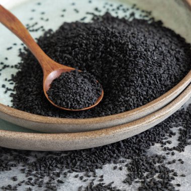 Hint baharatlı kimyon tabakası (nigella sativa ya da kalonji) tohumları, tahta kaşıkla gri masada, yakın mesafede. Geleneksel Asya tıbbı, sağlıklı ve vejetaryen gıda konsepti