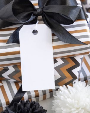 Boş dikey hediye etiketi ve siyah fiyonk var. Çizgili ve simge geometrik kağıda sarılı hediye kutuları, siyah ve beyaz dekorun yanında. Noel, Yeni Yıl, Doğum günü, Yıldönümü Modeli