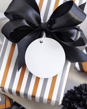 Yuvarlak boş hediye etiketi ve siyah fiyonk var. Siyah beyaz dekorun yanında çizgili geometrik kağıda sarılı hediye kutuları. Noel, Yeni Yıl, Doğum günü, Yıldönümü Modeli