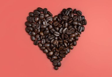 Pembe arka planda kavrulmuş kahve çekirdeklerinden yapılmış kalp. Kahvaltıyı, aşkı, enerjiyi, tazeliği veya aromayı temsil eder.