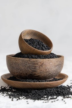Hint baharatlı kimyon (nigella sativa veya kalonji) tohumları beyaz masadaki ahşap kaselerde yakın plan. Geleneksel tıp, sağlıklı ve vejetaryen gıda konsepti.