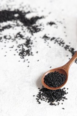 Tahta kaşık dolusu Hint baharatlı kimyon (nigella sativa veya kalonji) tohumları beyaz masaya kapanıyor. Geleneksel Asya tıbbı, sağlıklı beslenme, vejetaryen ve vejetaryen gıda konsepti