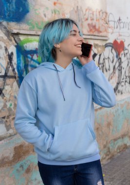 Mavi kapüşonlu, gülümseyen hippi kız cep telefonuyla konuşuyor, maket yapıyor. Grafiti duvarının yanında mavi saçlı bir genç. Ergenlik ve kar tanesi üretimi kavramı
