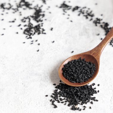 Tahta kaşık dolusu Hint baharatlı kimyon (nigella sativa veya kalonji) tohumları beyaz masaya kapanıyor. Geleneksel Asya tıbbı, sağlıklı beslenme, vejetaryen ve vejetaryen gıda konsepti
