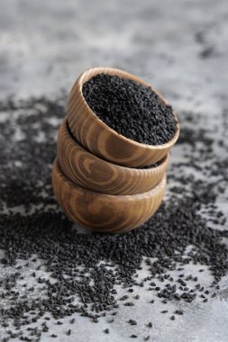 Hint baharatlı kimyon (nigella sativa veya kalonji) tohumları gri masadaki ahşap kaselerde yakın plan. Geleneksel tıp, sağlıklı ve vejetaryen gıda konsepti.