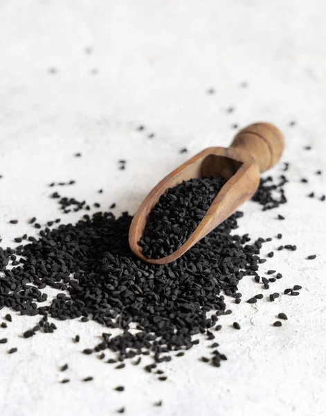 Tahta kepçe Hint baharatlı kimyon (nigella sativa veya kalonji) tohumları beyaz masaya yakın. Geleneksel Asya tıbbı, sağlıklı beslenme, vejetaryen ve vejetaryen gıda konsepti