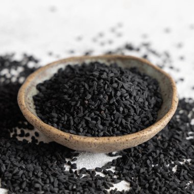 Hint baharatlı kimyon (nigella sativa veya kalonji) tohumları kaptaki gri masada yakın plan. Geleneksel tıp, sağlıklı ve vejetaryen gıda konsepti.