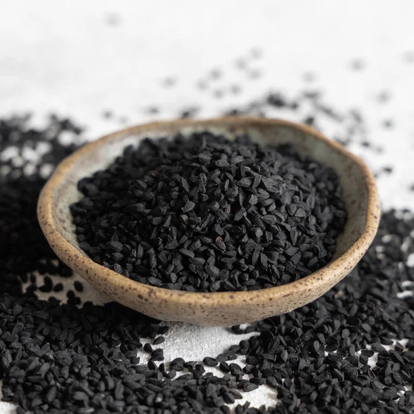 Hint baharatlı kimyon (nigella sativa veya kalonji) tohumları kaptaki gri masada yakın plan. Geleneksel tıp, sağlıklı ve vejetaryen gıda konsepti.