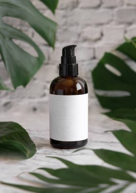 Kahverengi bir pompa dağıtıcısı ve tropikal canavar yaprakları mermer masaya yakın. Marka ambalaj modeli. Cilt bakım ürünü. Doğal bitkisel kozmetik uzmanları