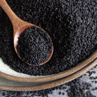 Hint baharatlı kimyon tabakası (nigella sativa ya da kalonji) tohumları, tahta bir kaşıkla gri masanın üzerinde, üst manzara. Geleneksel Asya tıbbı, sağlıklı ve vejetaryen gıda konsepti