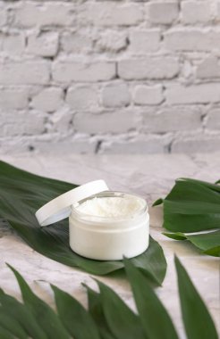 Mermer masada beyaz kavanoz ve canavar yaprakları var. Kapatın. Marka ambalaj modeli. Cilt bakım ürünleri, krema ya da tereyağı. Doğal malzemeden ev yapımı bitkisel kozmetik.