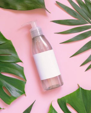 Pembe üst manzaralı tropik yapraklar arasında şeffaf bir şişe. Dağıtıcı ambalaj modeli. Doğal bitkisel kozmetik konsepti - cilt bakım ürünü, temizleyici veya ton