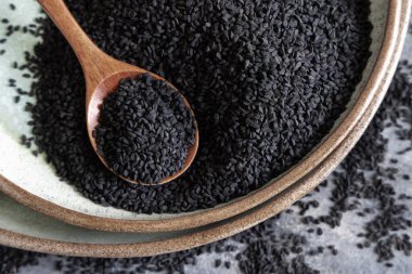 Hint baharatlı kimyon tabakası (nigella sativa ya da kalonji) tohumları, tahta bir kaşıkla gri masanın üzerinde, üst manzara. Geleneksel Asya tıbbı, sağlıklı ve vejetaryen gıda konsepti