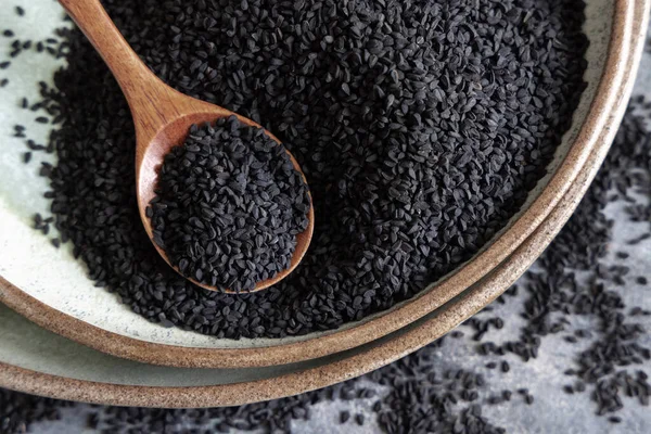 Hint baharatlı kimyon tabakası (nigella sativa ya da kalonji) tohumları, tahta bir kaşıkla gri masanın üzerinde, üst manzara. Geleneksel Asya tıbbı, sağlıklı ve vejetaryen gıda konsepti