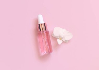 Açık pembe damlalı şişe, beyaz orkide çiçeğinin yanında açık pembe, üst manzara, maket. Cilt bakım ürünü, Aromatik yağ ya da serum. Egzotik kozmetik ürünler, pastel minimumda kompozit.