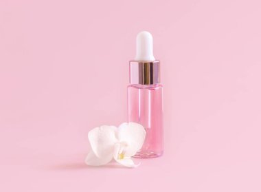 Açık pembe damlalı şişe, beyaz orkide çiçeğinin yanında açık pembe, yakın plan, maket. Cilt bakım ürünü, Aromatik yağ ya da serum. Egzotik kozmetik ürünler, pastel minimumda kompozit.
