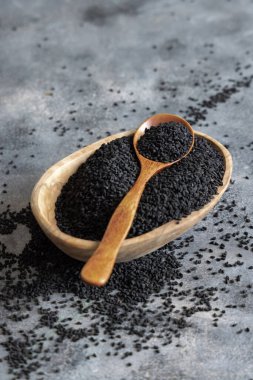 Hint baharatlı kimyon (nigella sativa veya kalonji) tohumları kasede, gri masada kaşıkla fotokopi alanı ile yakın çekim yapar. Geleneksel tıp, sağlıklı ve vejetaryen gıda konsepti.