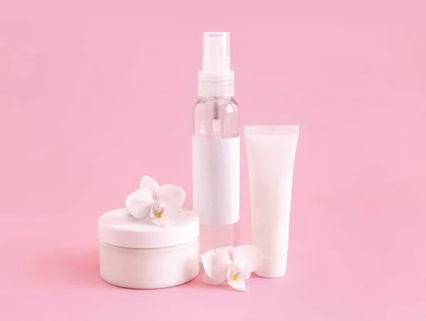 White cosmetic jar, tube and bottle near white orchid flower on light pink, close up, mockup. Skincare beauty product, cream or lotion. Exotic natural cosmetics, pastel minimal compositio