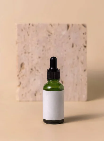 stock image Green glass dropper bottle near beige travertine stone on light yellow, close up, mockup. Skincare beauty product, serum or lotion. Handmade natural cosmetics, trendy minimal compositio