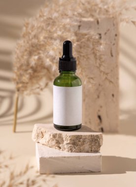 Travertin taşının üzerinde yeşil damlacık şişesi açık sarıdaki kuru otların yanında, yakın plan, maket. Cilt bakım ürünü. Doğal kozmetikler. Boho bileşimi