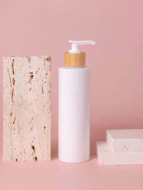 Beyaz bir pompa şişesi bej travertin taşının yanında açık pembe üzerinde, yakın plan, maket. Cilt bakım ürünü. Doğal kozmetik ürünleri, losyon ya da temizleyici. En düşük kompozitif