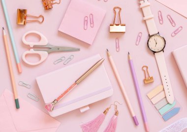 Pembe okul aksesuarları ve pastel pembe arka plan manzaralı kırtasiye malzemeleri. Not defteri, makas, kalem, kalem, yapışkan kağıt, ataç ve saati olan kız işyeri. Okul konseptine dönelim.