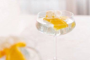 Turuncu beyaz orkide çiçeğiyle süslenmiş şampanya kadehinde buz küpleriyle şeffaf bir kokteyl. Barda tropik bir içki. Yaz tatili havası