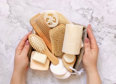 Elleri doğal deri ve saç bakım aksesuarlarını mermer masa manzarası üzerinde tutuyor. Kopya alanı. Doğal güzellik ürünleri